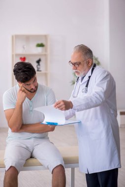 Genç erkek hasta yaşlı erkek doktoru ziyaret ediyor.
