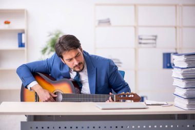 Genç erkek çalışan işyerinde gitar çalıyor.