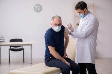 Yaşlı bir erkek hasta aşıyla genç bir doktoru ziyaret ediyor.