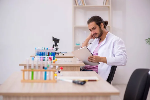 Ung manlig kemist sitter vid skrivbordet i klassrummet — Stockfoto
