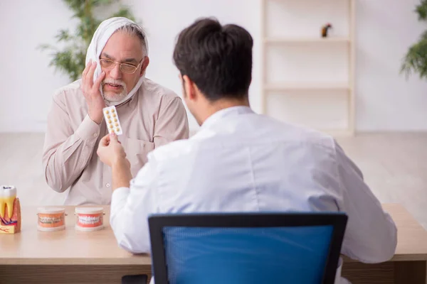 Viejo paciente masculino que visita al joven dentista médico masculino — Foto de Stock