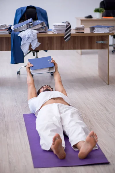 Joven empleado masculino haciendo ejercicios deportivos en la oficina —  Fotos de Stock