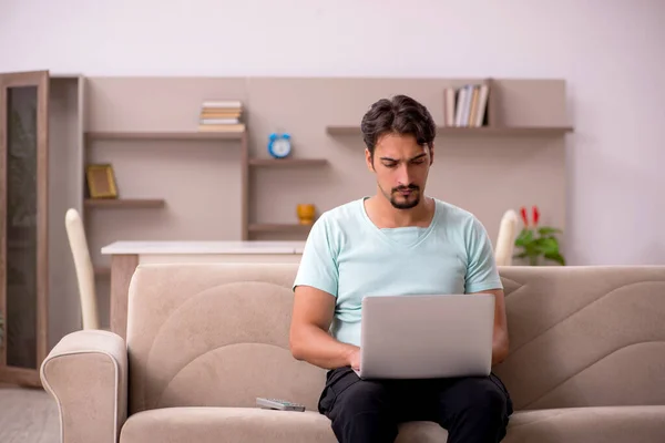 Mladý muž sedí na pohovce s počítačem doma — Stock fotografie