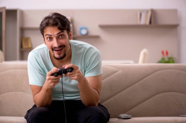 Genç adam evde joystick oynuyor.