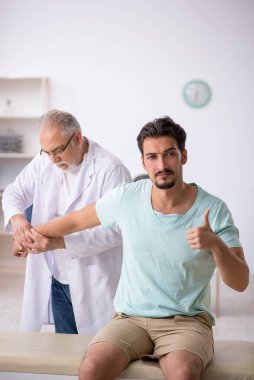 Genç erkek hasta yaşlı erkek doktoru ziyaret ediyor.