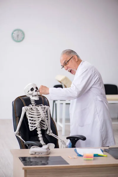 Old male doctor with skeleton in the clinic — Stock Photo, Image