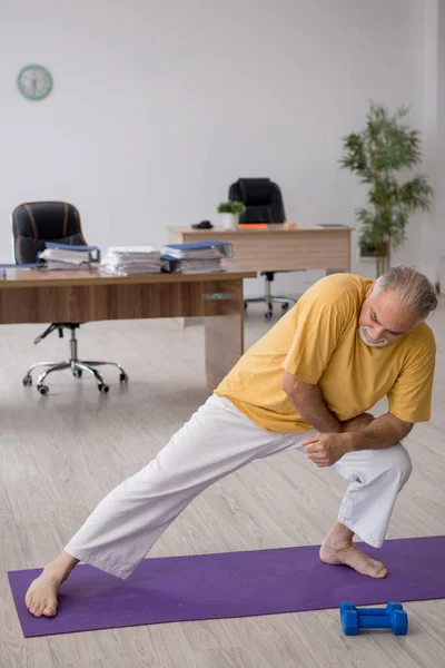 Velho empresário empregado fazendo exercícios esportivos no escritório — Fotografia de Stock