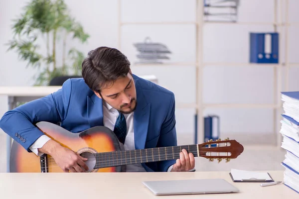 Joven empleado masculino tocando guitarra en el lugar de trabajo — Foto de Stock