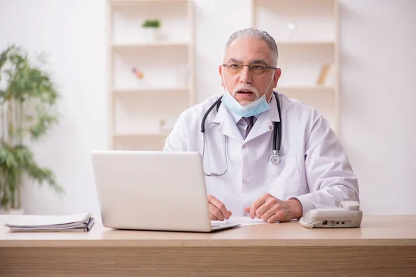 Yaşlı erkek doktor salgın sırasında klinikte çalışıyor. — Stok fotoğraf