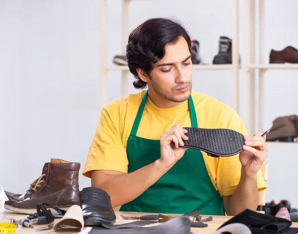 Молодой человек чинит обувь в мастерской — стоковое фото