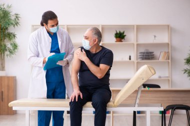 Yaşlı adam covid-19 aşı konseptinde genç doktoru ziyaret ediyor.