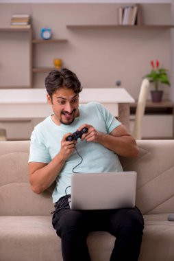 Genç adam evde joystick oynuyor.