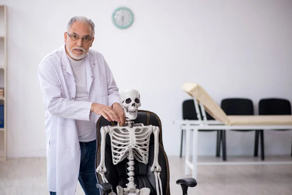 Gammal manlig läkare med skelett på kliniken — Stockfoto