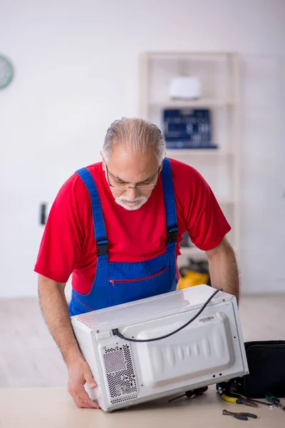 Old repairman repairing oven at workshop — Stock Photo, Image