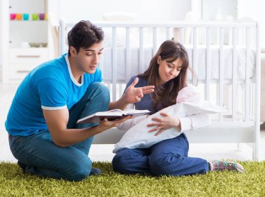 Yeni doğmuş bebekleriyle halıda oturan genç ebeveynler.