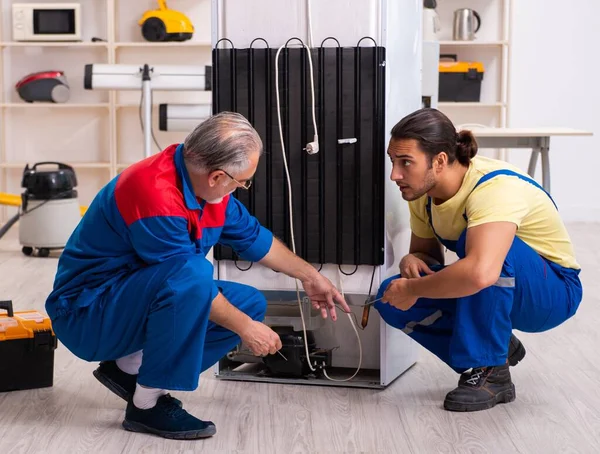 Two contractors repairing fridge at workshop