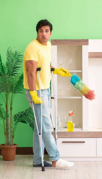 Injured man on crutches cleaning house