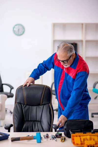 Eski erkek tamirci ofis sandalyesini tamir ediyor. — Stok fotoğraf