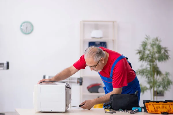Old repairman repairing oven at workshop — Stock Photo, Image