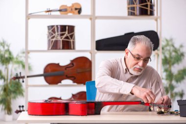Yaşlı erkek tamirci iş yerinde müzik aletlerini tamir ediyor.