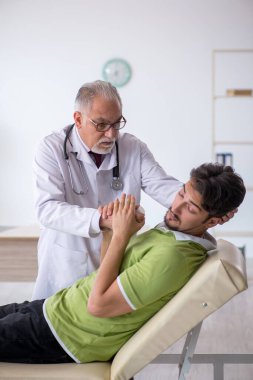 Genç erkek hasta yaşlı erkek doktoru ziyaret ediyor.