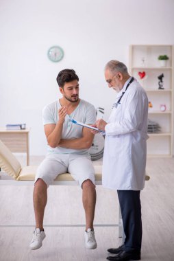 Genç erkek hasta yaşlı erkek doktoru ziyaret ediyor.