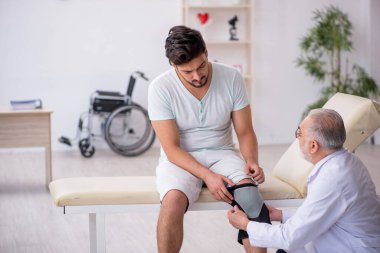 Genç bacağı yaralı hasta yaşlı doktoru ziyaret ediyor.