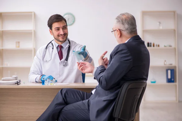 Старый бизнесмен посещает молодого врача-мужчину в рамках концепции вакцинации — стоковое фото