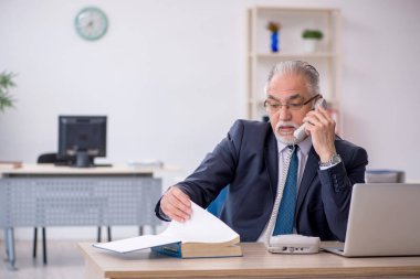 İş yerinde yaşlı bir erkek çalışan telefonda konuşuyor.