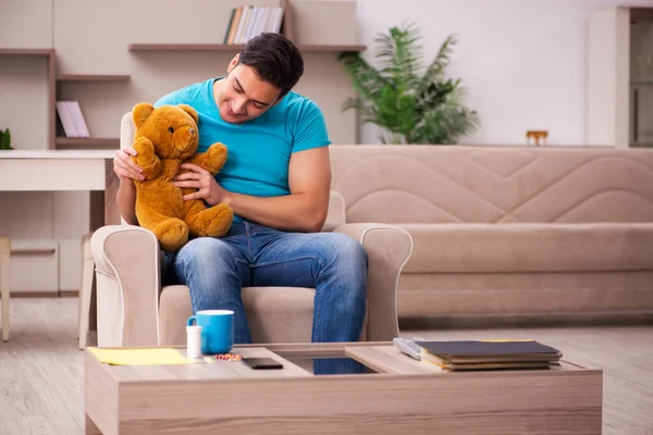 Genç adam evde ayı oyuncağıyla oturuyor. — Stok fotoğraf
