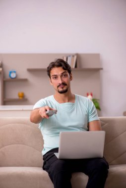 Genç adam evde televizyon izliyor.