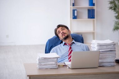 Genç bir erkek çalışan ve ofiste çok fazla iş var.