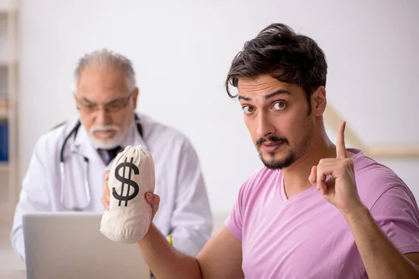 Junge männliche Patienten besuchen alten Arzt gegen Bezahlung — Stockfoto