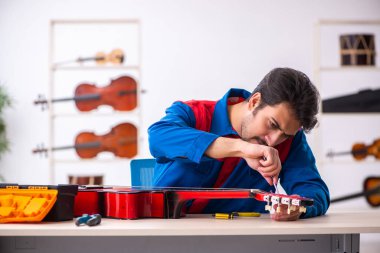Genç erkek tamirci işyerinde müzik aletlerini tamir ediyor.