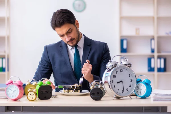 Joven empleado de negocios comiendo despertador-reloj —  Fotos de Stock