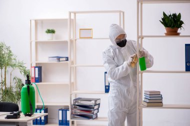 Young male contractor disinfecting office during pandemic