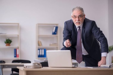 Eski erkek çalışan işyerinde oturuyor.