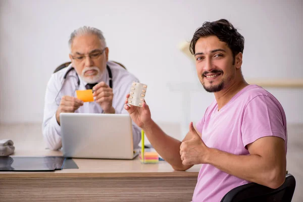 Jovem paciente masculino visitando velho médico masculino — Fotografia de Stock