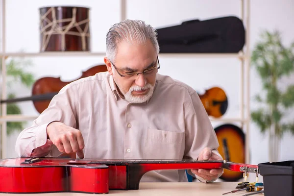 Viejo reparador masculino reparando instrumentos musicales en el lugar de trabajo — Foto de Stock