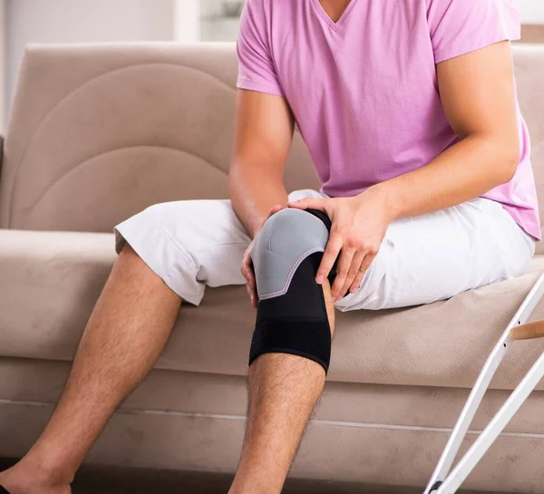 Молодой человек с травмой колена выздоравливает дома — стоковое фото