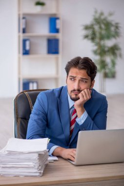 Genç bir erkek çalışan ve ofiste çok fazla iş var.