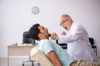 Genç erkek hasta yaşlı erkek doktoru ziyaret ediyor.