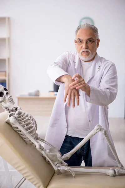 Старий лікар зі скелетом у клініці — стокове фото