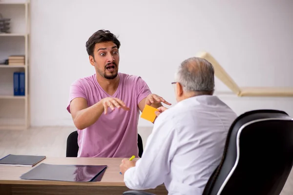 Jonge mannelijke patiënt bezoekt oude mannelijke arts — Stockfoto