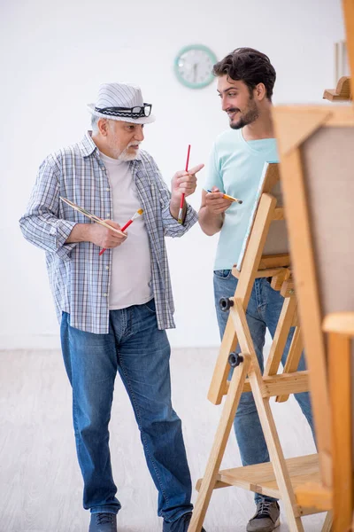Velho pintor ensinando jovem estudante no estúdio — Fotografia de Stock