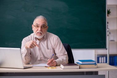 Tahtanın önünde yaşlı bir erkek öğretmen.