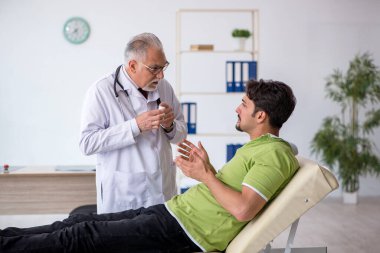 Genç erkek hasta yaşlı erkek doktoru ziyaret ediyor.