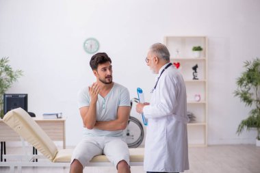 Genç erkek hasta yaşlı erkek doktoru ziyaret ediyor.