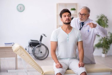 Genç erkek hasta yaşlı erkek doktoru ziyaret ediyor.