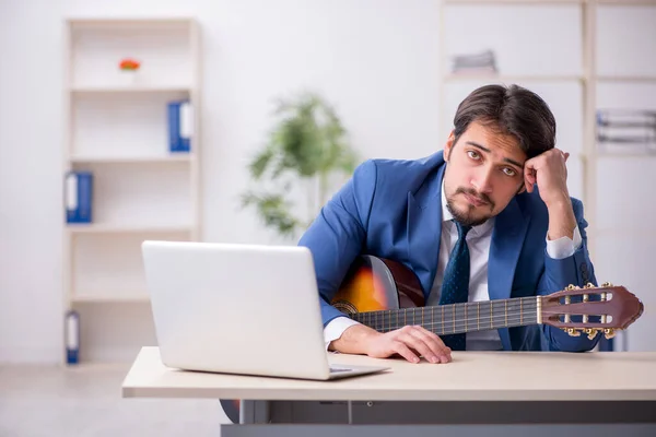 Jeune employé masculin jouant de la guitare sur le lieu de travail — Photo